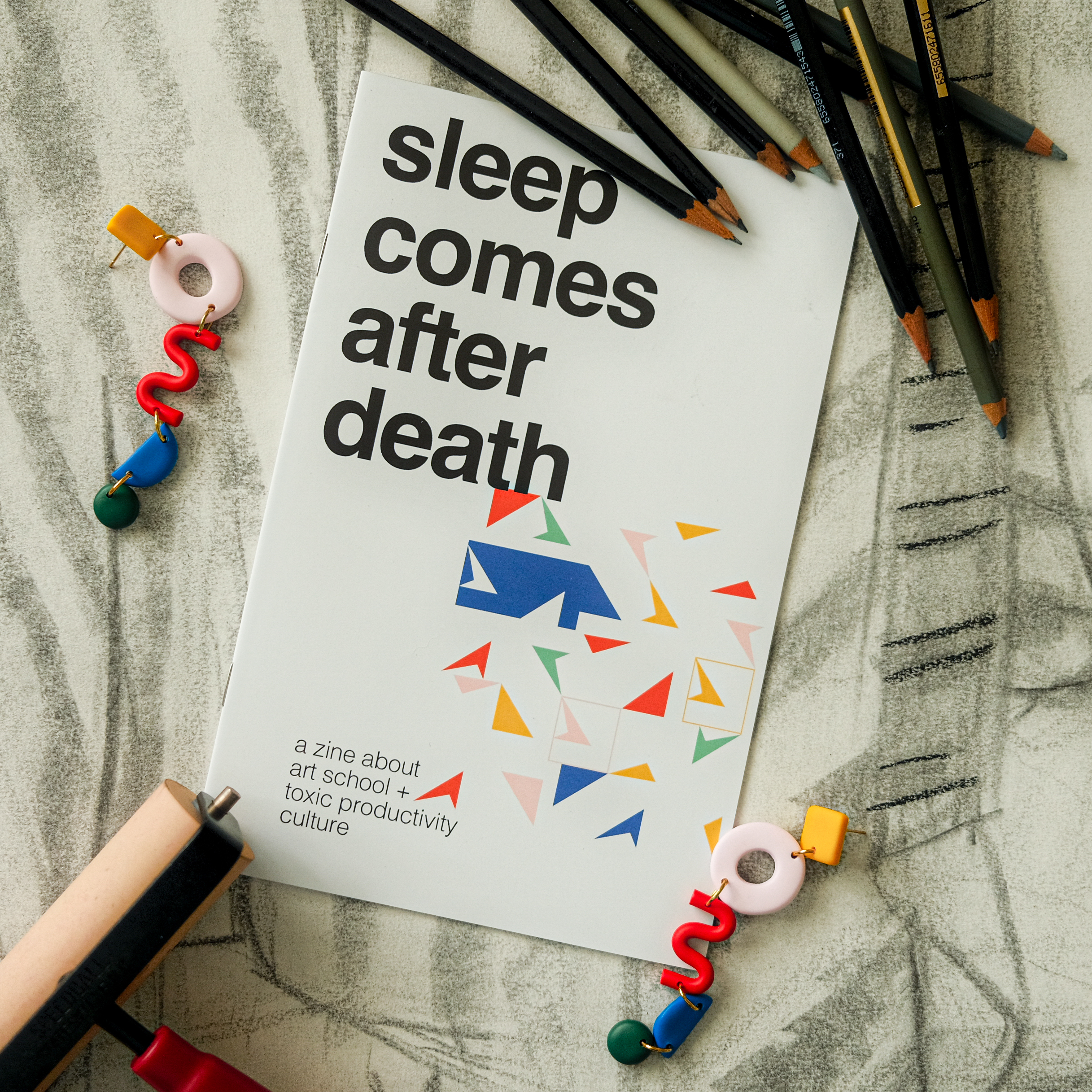 'Sleep Comes After Death' zine cover, a white page with the title written in lowercase, bold, black, san-serif letters. A colorful geometric design takes up a small amount of space. The caption 'a zine about art school + toxic productivity culture' is on the bottom of the cover in lowercase, skinny letters.